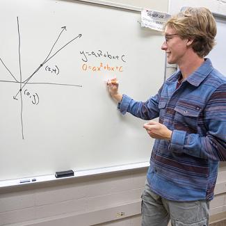UW-Platteville student standing at marker board working on equations