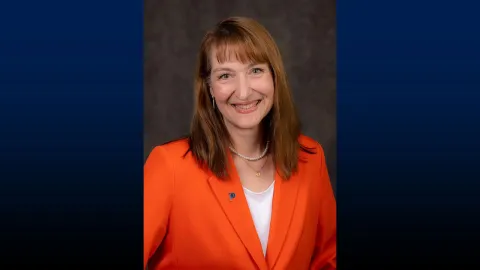 Headshot of UW-Platteville Chancellor Tammy Evetovich wearing an orange blazer on a blue background