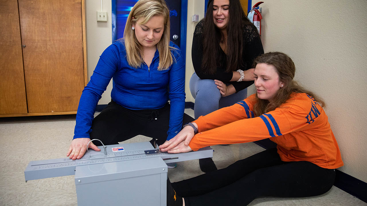 Brooke Kunkel, Monica Radtke, and Ann Larson demonstrate a sit-and-reach test which they used to assess flexibility in their study participants.