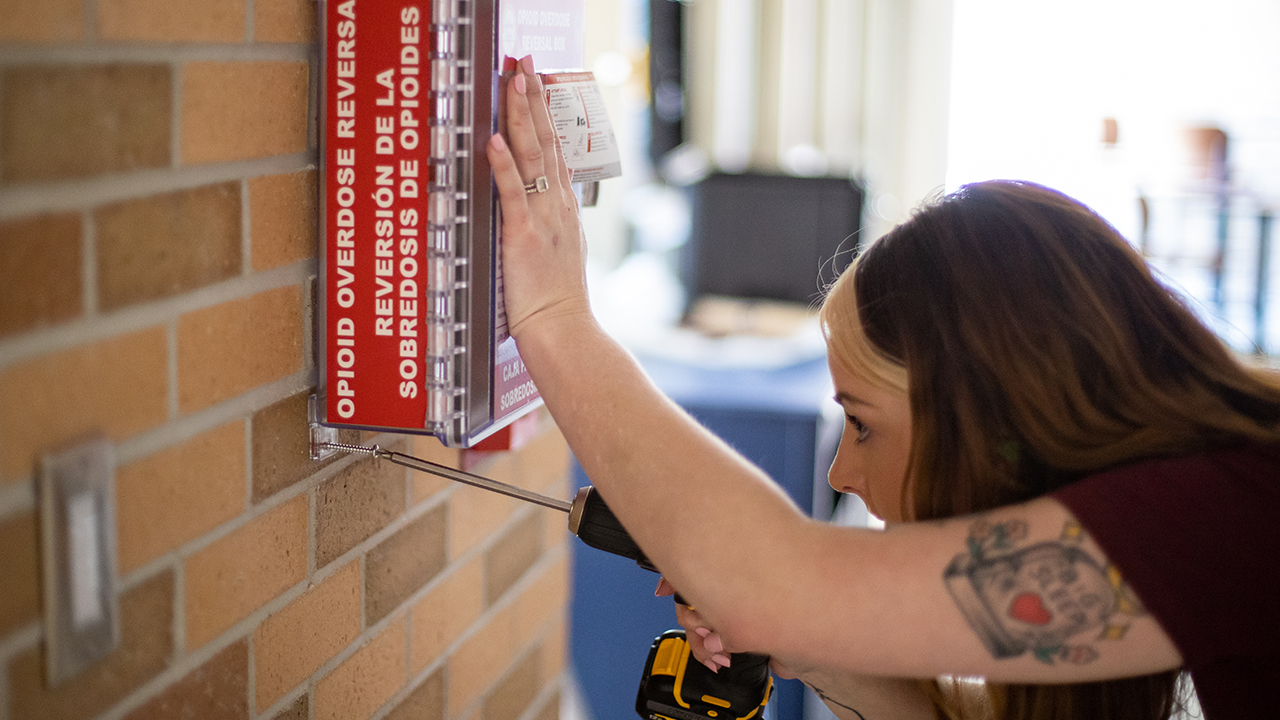 Meghan Vieth, from Wisconsin Voices for Recovery, installs a Nalox-Zone box in the Student Center.