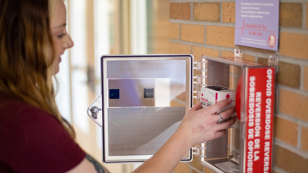 Meghan Vieth, from Wisconsin Voices for Recovery, installs a Nalox-Zone box in the Student Center.