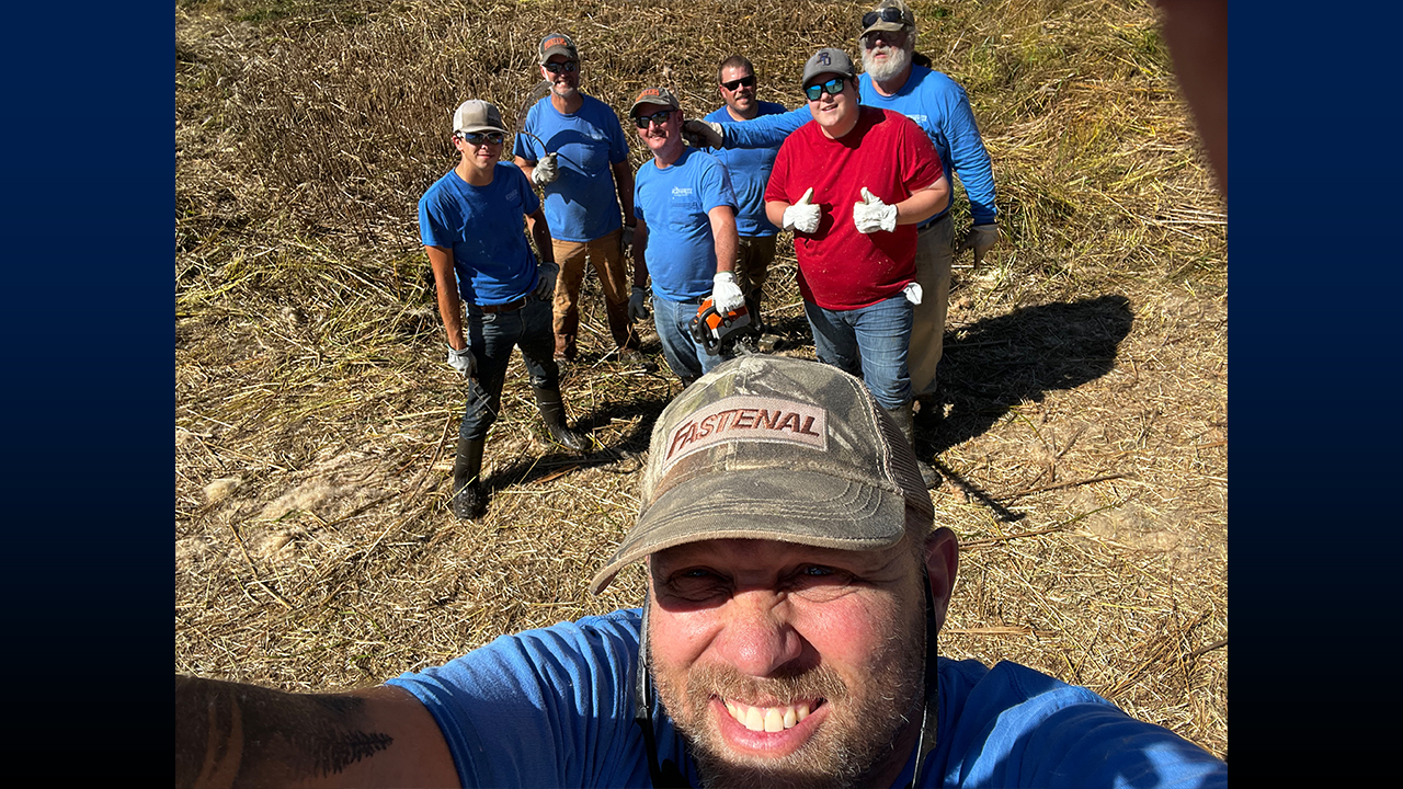 Schute, pictured in front with the grounds crew, working diligently to clean the retention ponds, ensuring a clean and well-maintained environment.