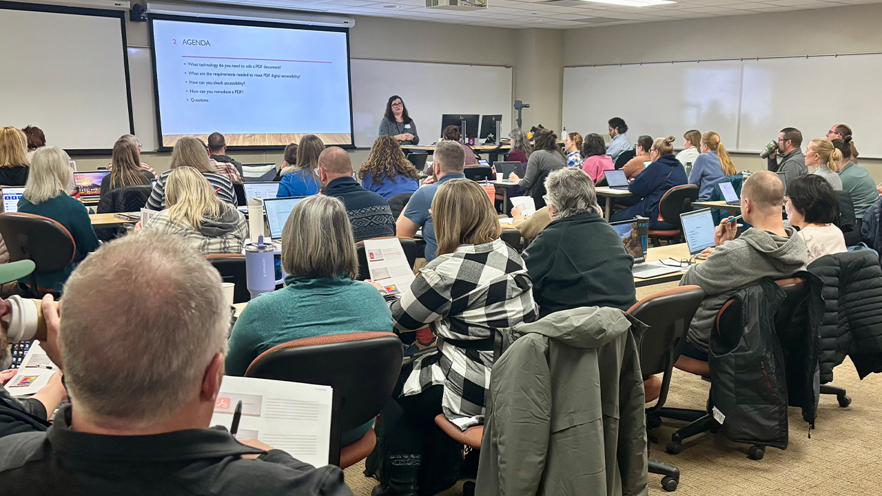 People in a room, looking at a screen on the wall during a lecture. 