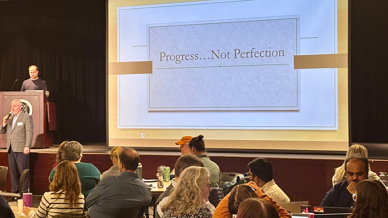 Speaker at podium with large screen in the background. 