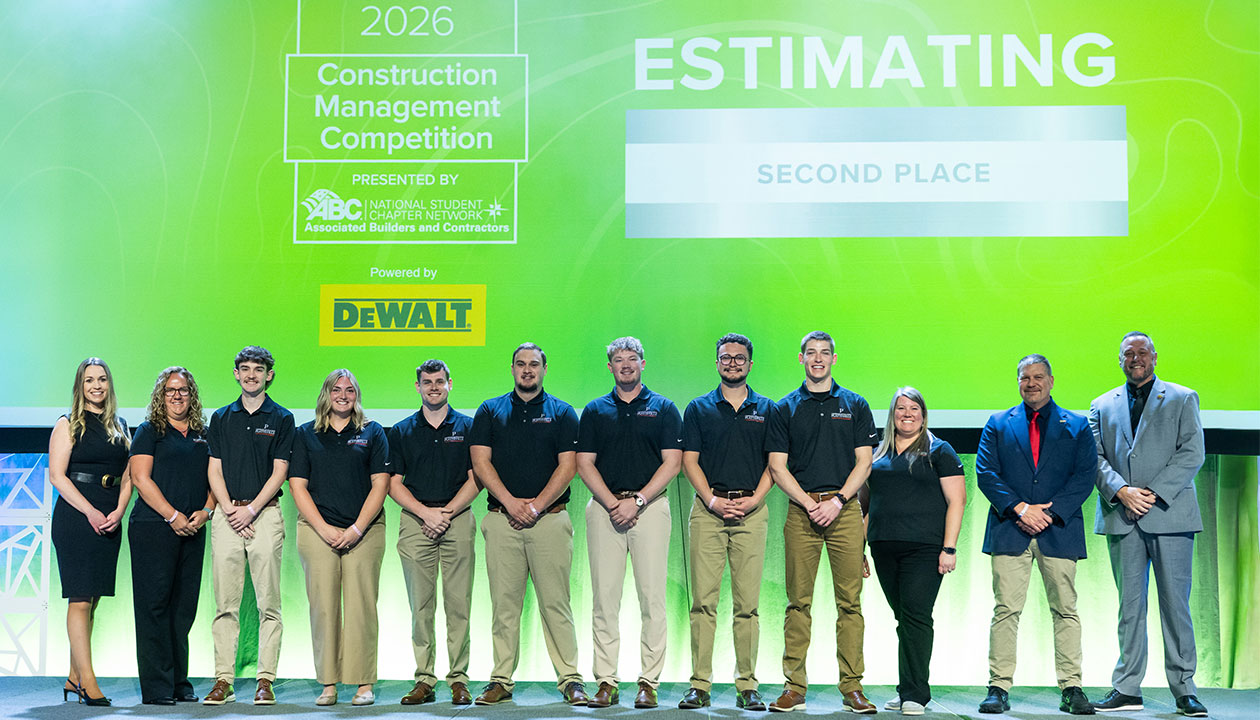 Large group of UW-Platteville students and faculty in front of green background while accepting an award