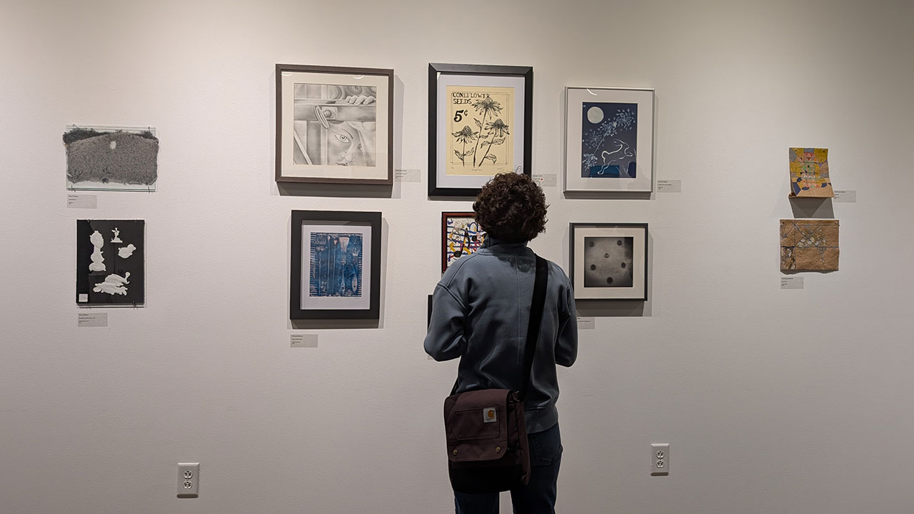 A student is facing a white wall in an art gallery, studying several pieces of art
