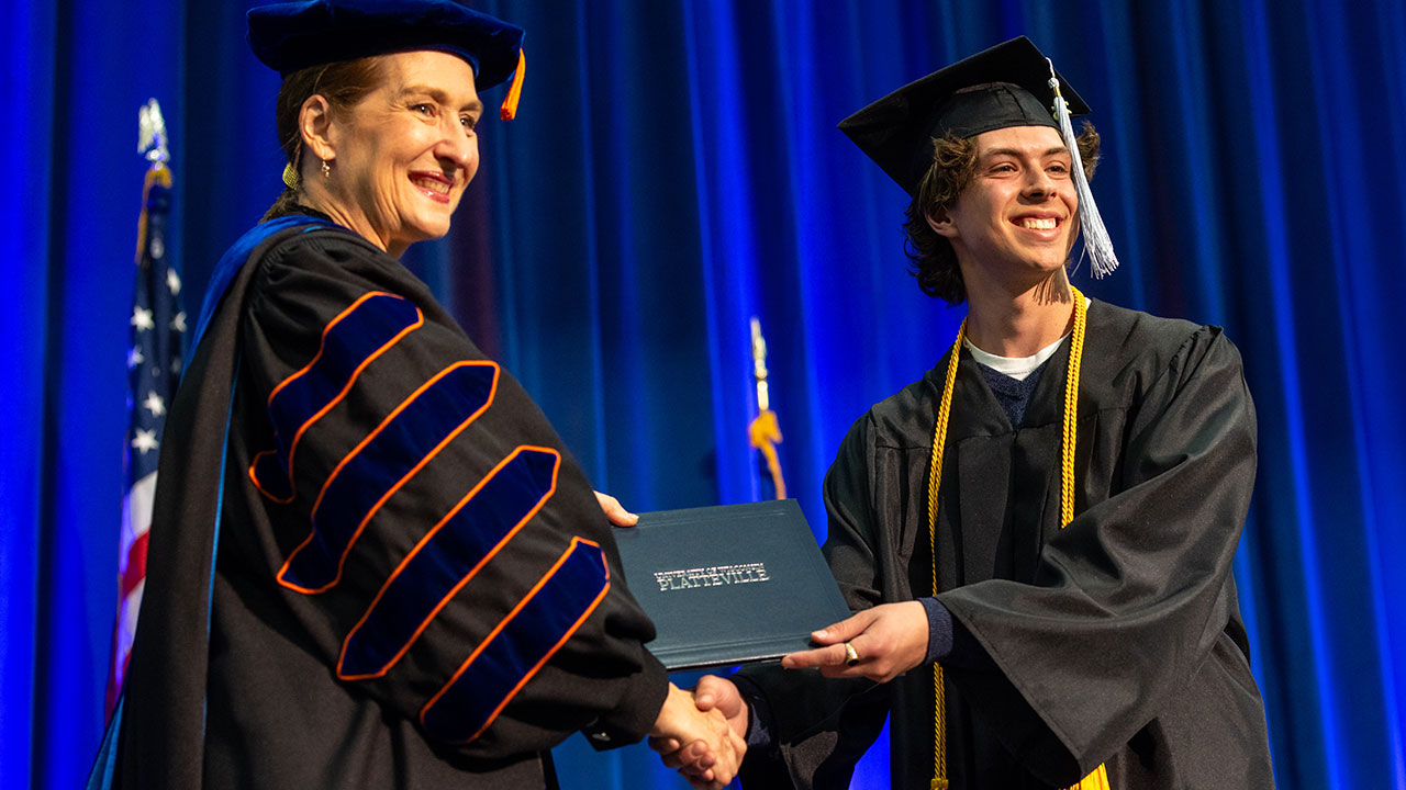 UW-Platteville student smiles while shaking Chancellor's hand when receiving diploma at Commencement.