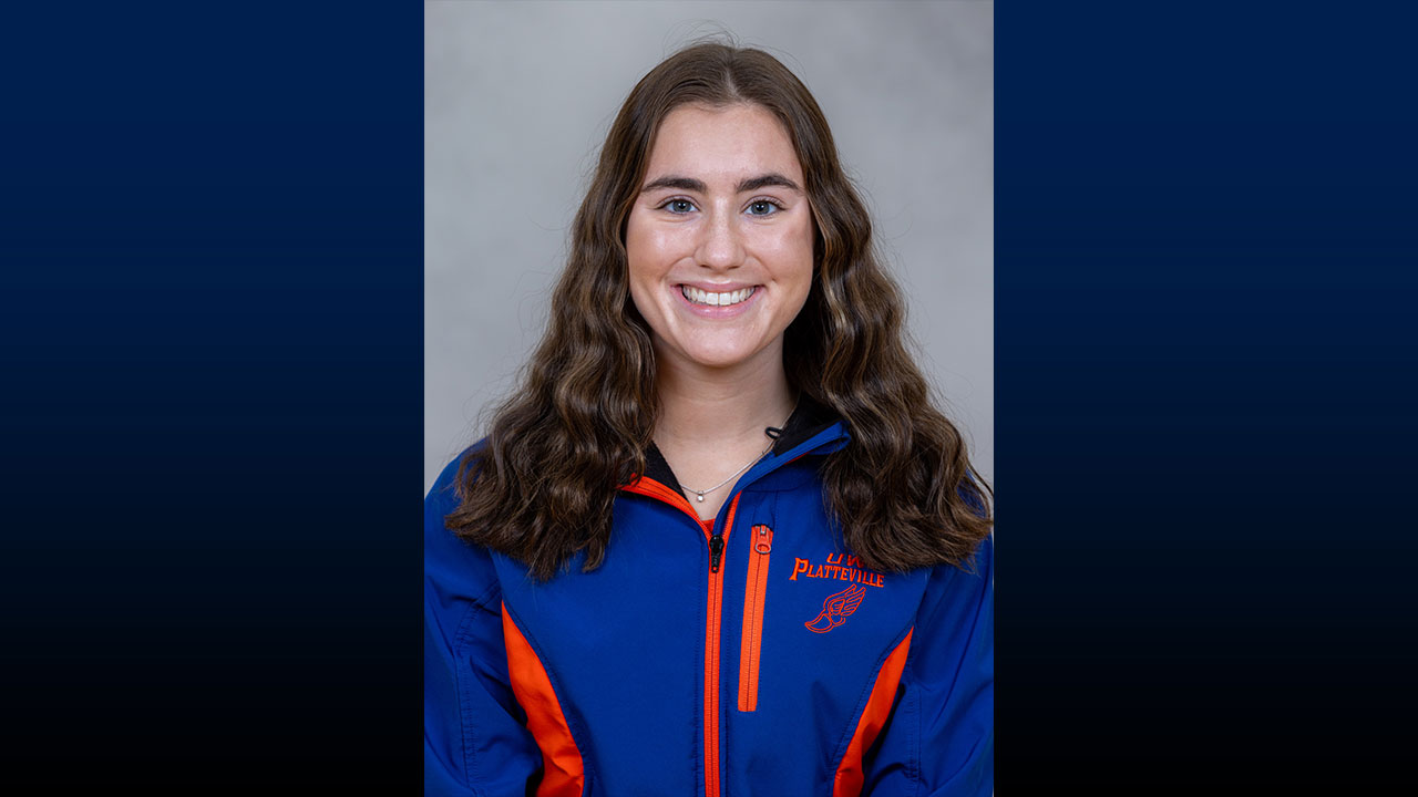 Headshot of a smiling female with long brown hair wearing an orange and blue jacket.