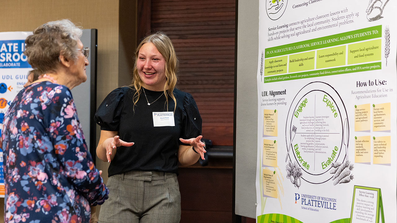 Two individuals talking in front of a large poster.