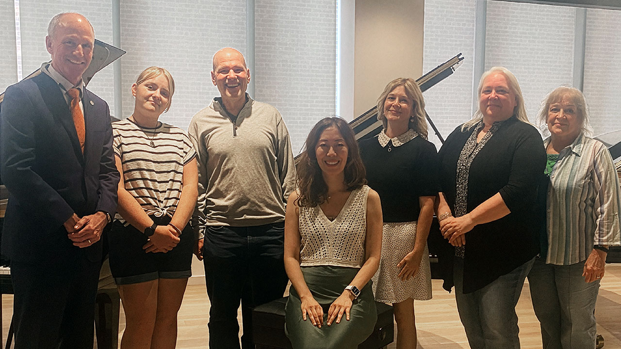 A group of individuals standing in a piano showroom in front of a Steinway piano.