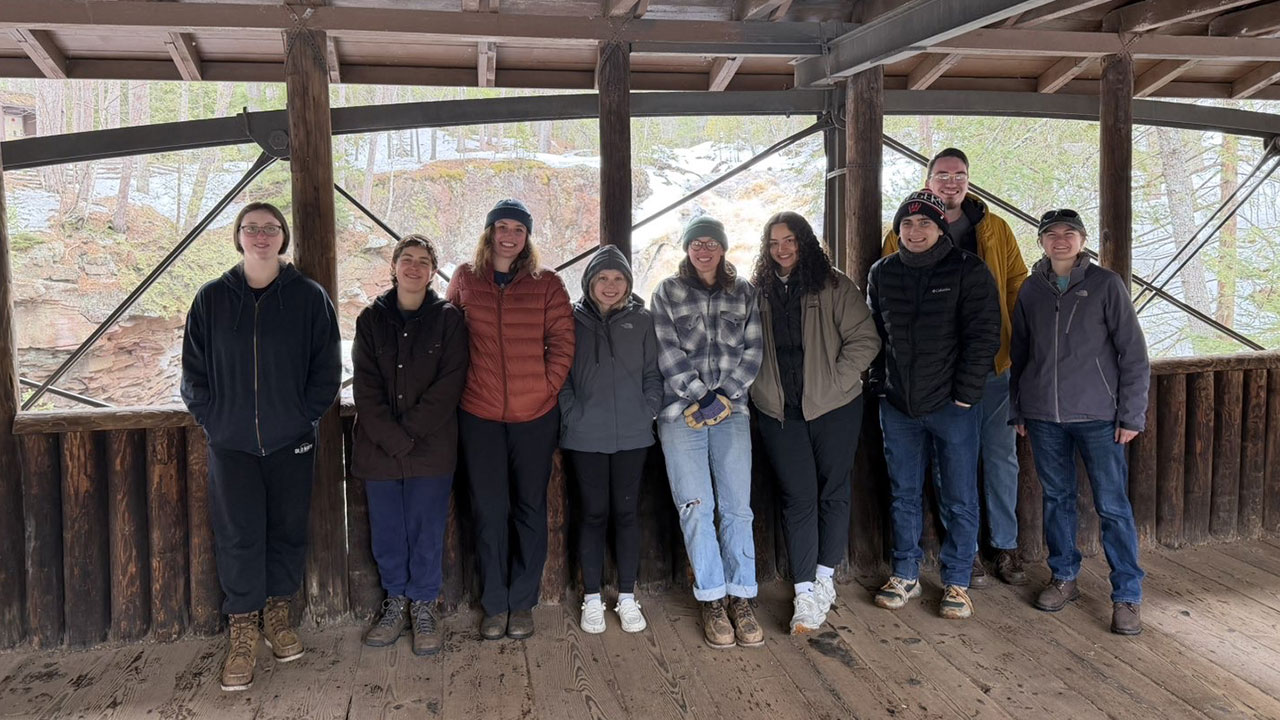 Students standing on covered bridge at Amnicon Falls State Park with a waterfall flowing in the background