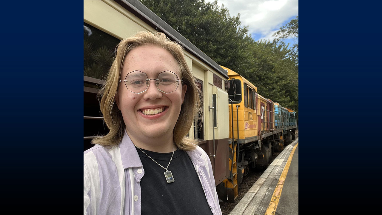 Individual smiling, with a several train cars in the background.