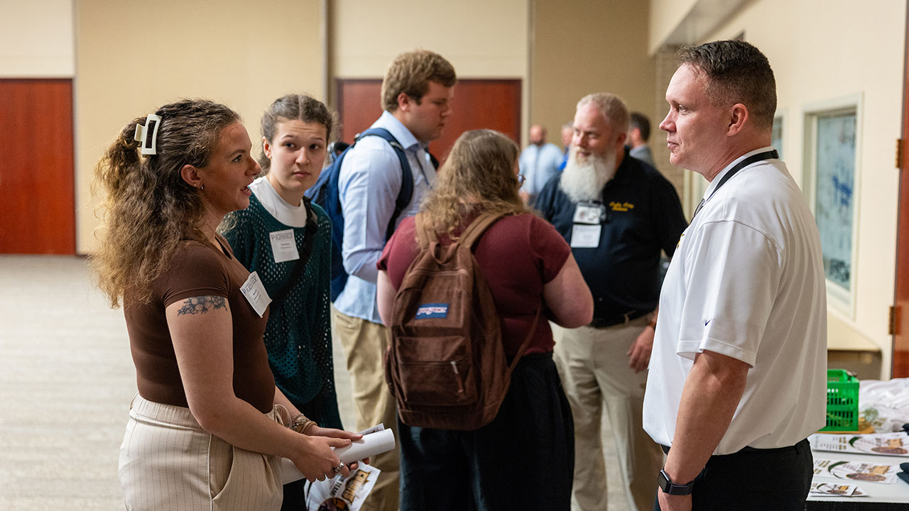Two individuals talking, with several others in the background.