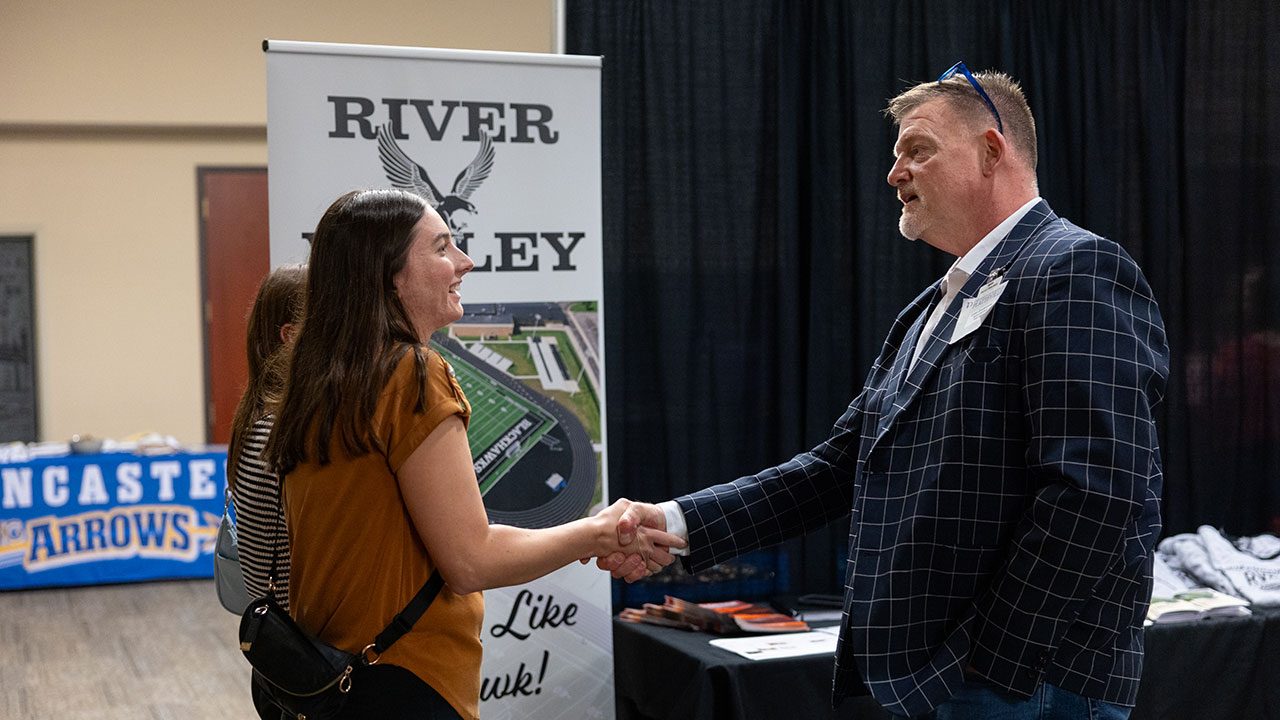A man in a blue suit shaking hands with a woman in a brown dress.