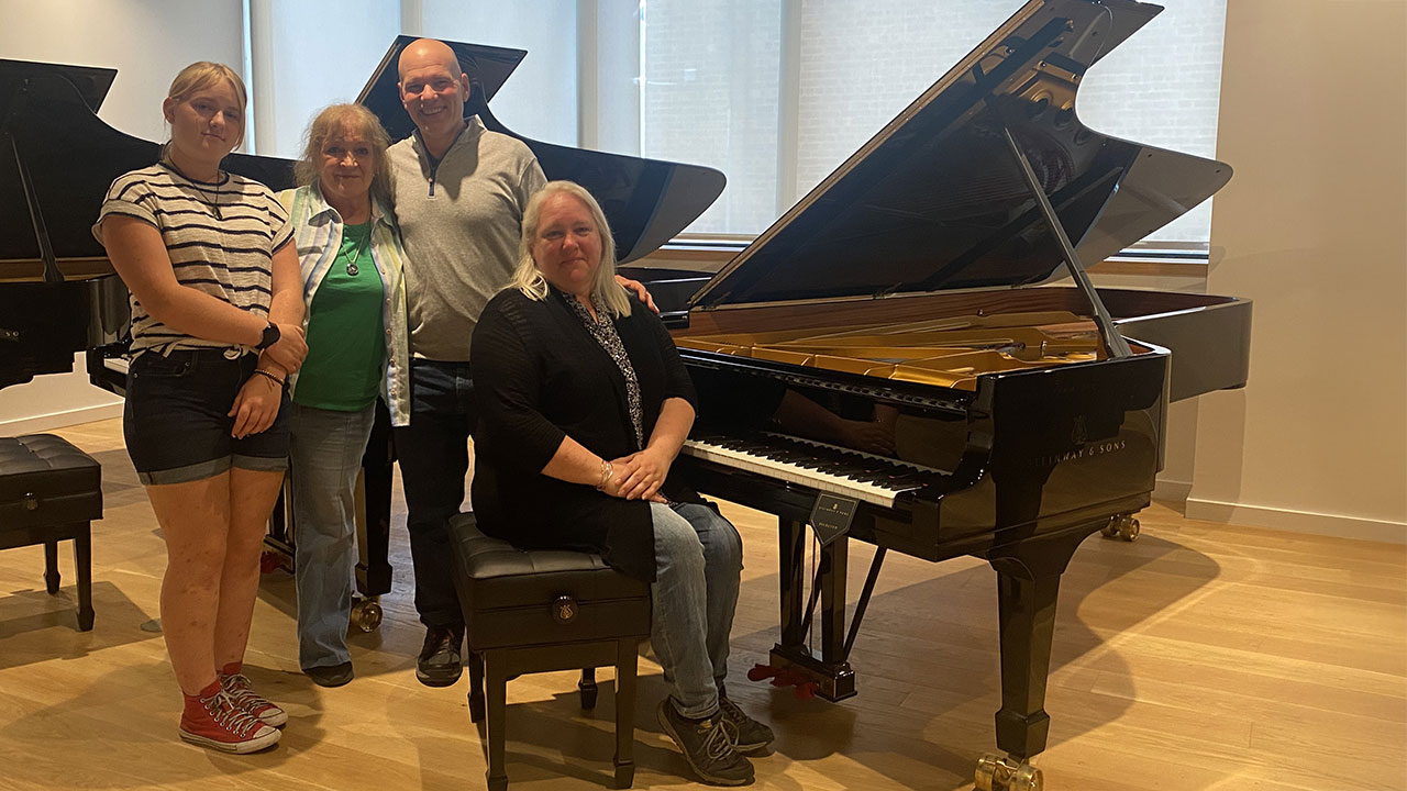 Woman sitting at a Steinway grand piano, with three individuals standing next to the piano.