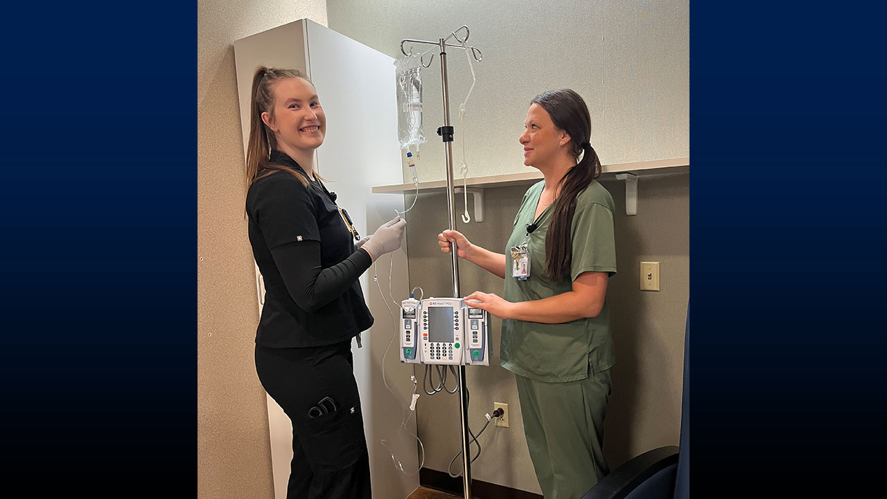 Two women in hospital scrubs, one holding an IV pole.