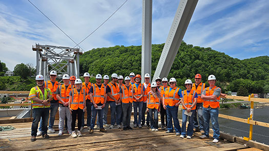 Group of students and faculty in orange safety vests standing on a bridge