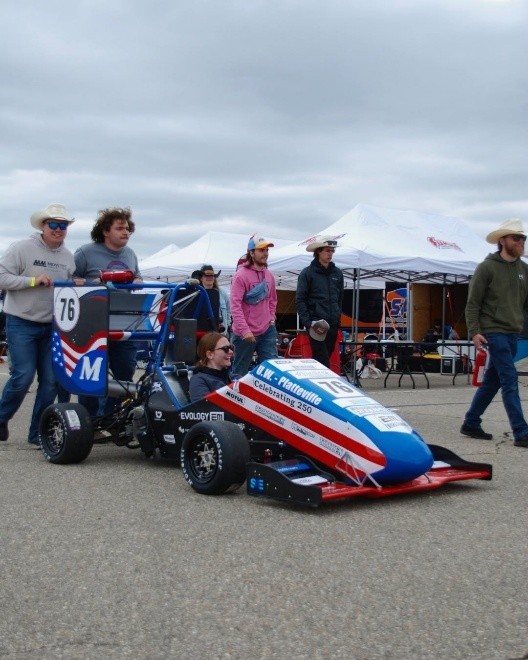 Members of the UW-Platteville Pioneer Racing team push their car into position at the 2026 Formula SAE Michigan competition.