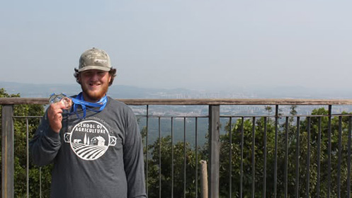 UW-Platteville junior Jakob Scheckel displays the medals he won in the 5th International Soil Judging Contest on front of a railing on top of China's Zhongshan Mountain in June. 