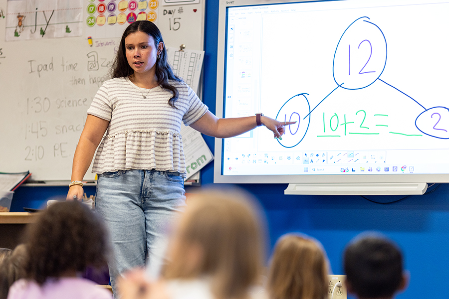 Educator interacting with a smartboard displaying an addition lesson