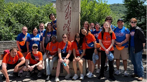 Large group of students in orange and blue shirts posing outdoors next to statue