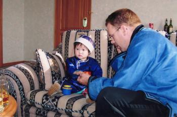 Phil Kerwin sits next to 20-month-old Agiimaa during the girl's adoption ceremony at an orphanage in Ulaanbaatar, Mongolia, in XX. Both Phil and Agiimaa are wearing traditioanl Mongolian garb.