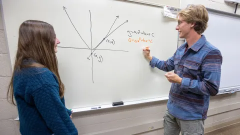 Students solving math problem on whiteboard.