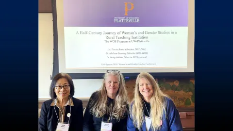 Three women smiling in front of a presentation screen.