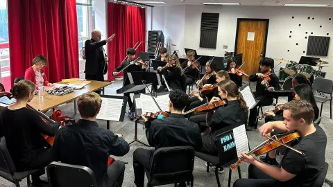 Music conductor directing a group of students playing instruments in a band room.