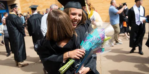 Graduate celebrating with family after the ceremony, one holding a bouquet and a diploma while embracing the other.
