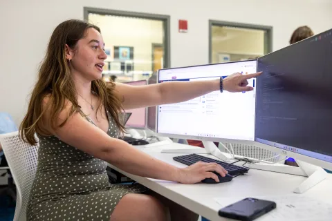 Person gesturing while explaining code displayed on a computer monitor during a collaborative session in a workspace.