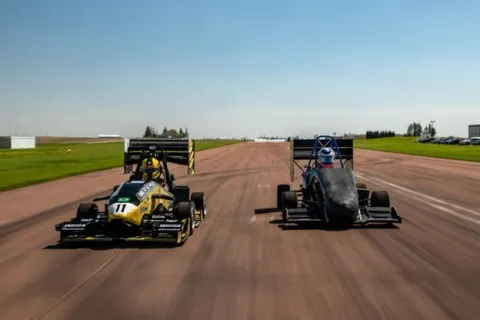 The University of Sao Paulo's yellow Formula SAE car races alongside UW-Platteville's car on a runway at the Lancaster Muncipal Airport in May.