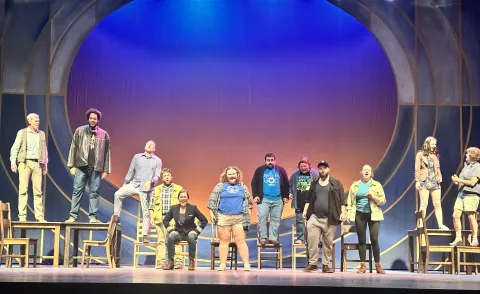 The cast of UW-Platteville's production of "Come From Away" stands on stage in front of a blue-and-orange backdrop during a rehearsal on July 19, 2026, at the Center for the Arts.
