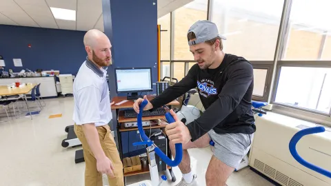 Athlete using a stationary bike with guidance from a trainer in a fitness facility.