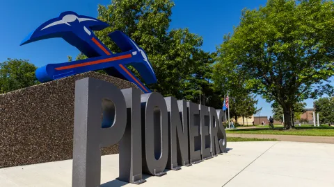 Signage for the Pioneers with a blue and orange logo of crossing tools in a park setting.