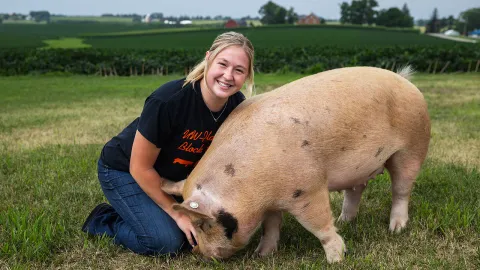 UW-Platteville senior Sophia Daugherty poses in a field at Pioneer Farm with a pig she plans to show at the Wisconsin State Fair.