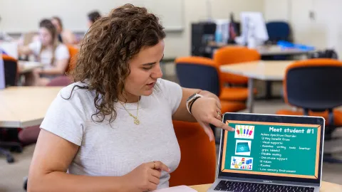 Student presenting a laptop screen that displays information about a student with autism spectrum disorder and recommended support strategies in a classroom setting.
