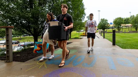 A student carrying a tote and a woman carrying a bag and a blanket walk on a UW-Platteville campus sidewalk.