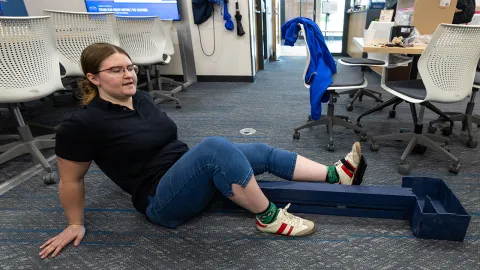 UW-Platteville engineering student Emily Milchuck on the floor in Sesquicentennial Hall demonstrating how an in-bed exercise machine she helped design works on Oct. 8, 2026.