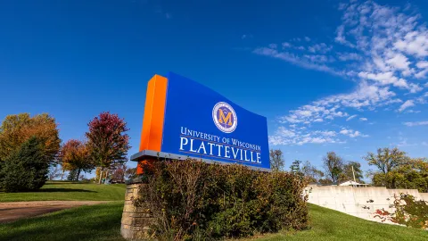 Sign for the University of Wisconsin Platteville located on a grassy area with trees and blue sky in the background.