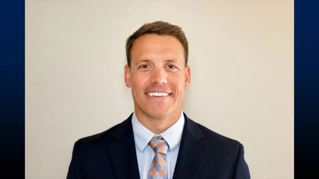 Headshot of smiling man in blue suit in front of a light background