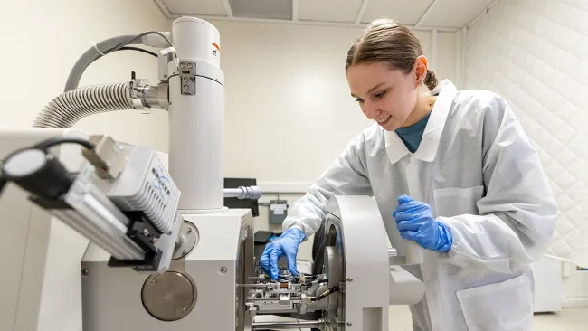 Researcher operating a scientific instrument in a lab setting while wearing gloves and a lab coat.