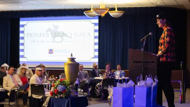 Woman standing at a podium, presenting to a room of seated guests