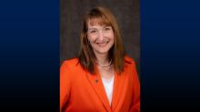 Headshot of UW-Platteville Chancellor Tammy Evetovich wearing an orange blazer on a blue background