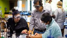 Group of students and a teacher collaborating on a science experiment in a laboratory setting.