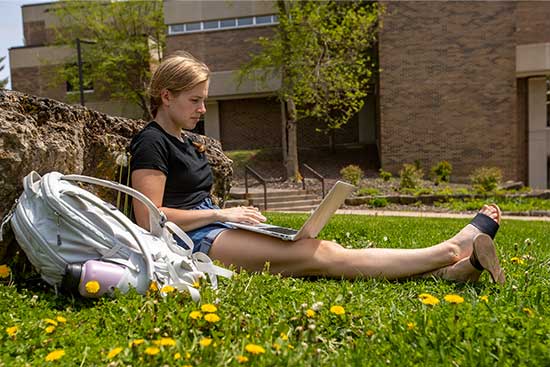 A focused UW-Platteville student is in the grass, working diligently on a laptop.