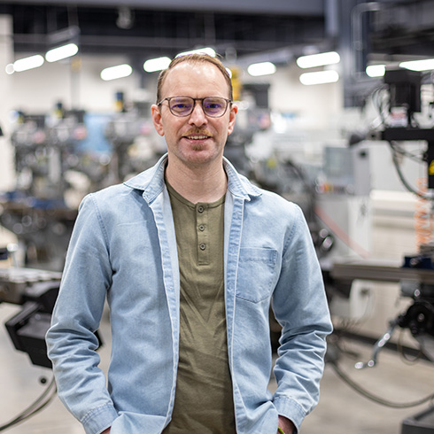 Matthew Alexander Ashauer, ’26, stands in the middle of a manufacturing floor.