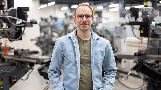 Matthew Alexander Ashauer, ’26, stands in the middle of a manufacturing floor.