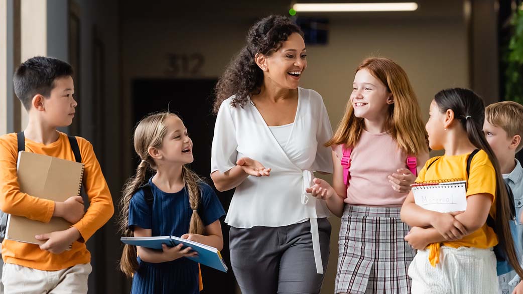 Group of elementary students listen enthusiastically to their principal as they walk down hallway
