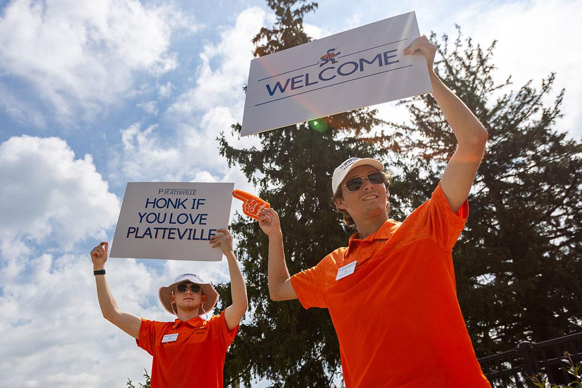 Two UW-Platteville students in orange shirts holding welcome signs on move in day